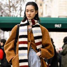 a model wears a brown coat with a striped scarf