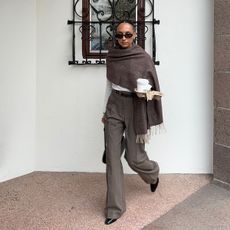 Ingrid wears a brown scarf, white top, brown pinstripe trousers, black flats, and black sunglasses.