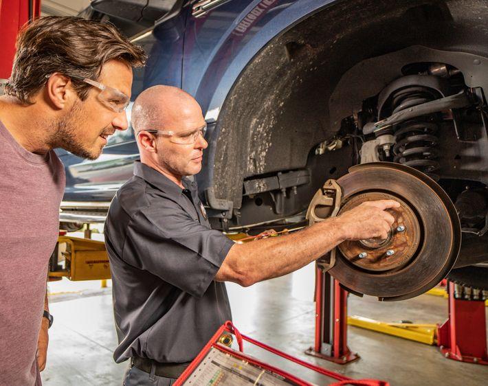 Tires Plus technician explains brake service to male customer wearing protective eye gear 