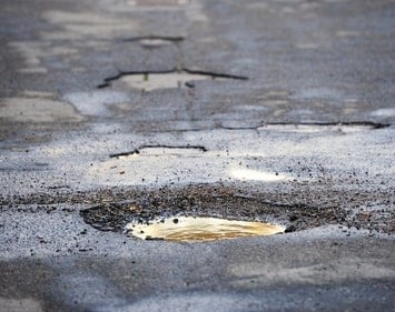 Pothole riddled asphalt street that are wet with murky rain water